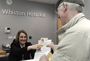 Photograph of a female receptionist dealing with a male visitor at Whiston Hospital